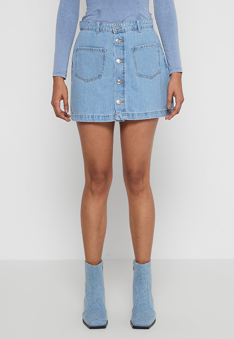 Mini-jupe en denim bleu clair avec un devant à cinq boutons, deux poches plaquées et un léger effilochage. Associée à des bottes de cheville bleu clair assorties.