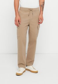 Pantalons cargo beiges en tissu mélangé coton, dotés d'une taille élastique avec cordon de serrage, de poches latérales et d'une coupe décontractée.