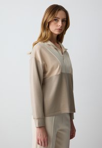 Beige zip-up sweatshirt met contrasterende panelen, relaxte pasvorm, lange mouwen en cuffs aan de onderkant. Zachte stof met een subtiele glans.