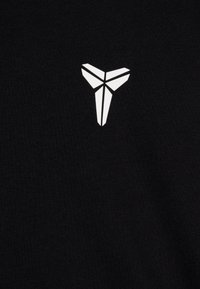 Juodas medvilnės marškinėliai su geometriniu baltu logotipu viduryje, sudarytu iš trikampių formų. Medžiaga turi tekstūrinį paviršių.