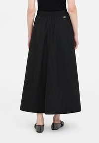 Gonna nera alla caviglia con vita elasticizzata e dettagli di cuciture sottili. Realizzata in tessuto leggero. Indossata con scarpe basse con motivo.