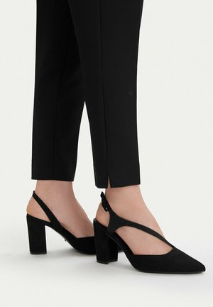 Czarne buty na wysokim obcasie typu slingback z szpiczastymi noskami, noszone z czarnymi, krótko przyciętymi spodniami z małymi rozcięciami po bokach przy kostkach.