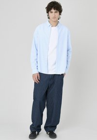 Chemise button-up rayée bleu clair sur un t-shirt blanc, associée à un pantalon ample rayé bleu foncé et des baskets noires.