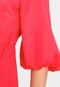 Světlé růžové šaty se strukturovaným designem, s nabíraným rukávem a staženým pasem. Hladká textilie a minimální detaily.