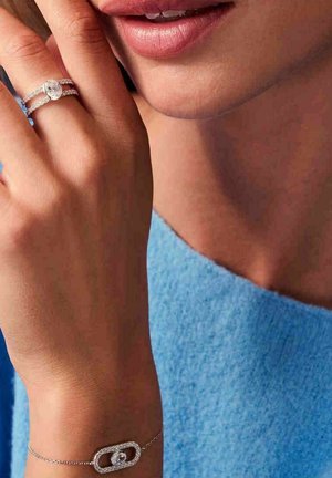 Sølvring med en oval sten, prydet med en funklede ring, samt et armbånd med en oval vedhæng, begge fremvist mod en blå baggrund.