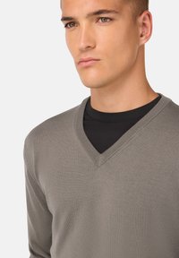 Grauer V-Ausschnitt-Pullover aus strukturiertem Strickstoff, über einem schwarzen Hemd getragen. Verfügt über einen regulären Schnitt und gerippte Bündchen.