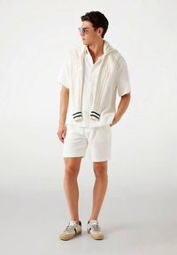 White short-sleeve shirt with a textured pattern, paired with matching shorts. A knitted white sweater is draped over the shoulders.