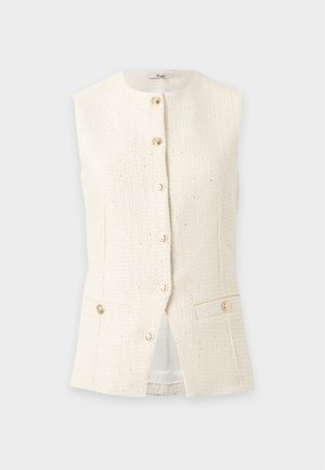 Donna snella con gilet bianco texturizzato abbottonato sopra una camicetta bianca con maniche a sbuffo, pantaloni neri a gamba larga e tacchi bianchi slingback, in piedi.