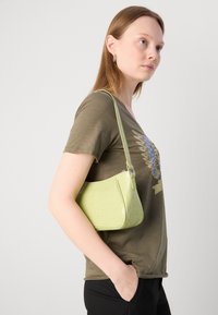 Lichtgroene, faux krokodillenleren handtas met een gebogen vorm, korte schouderriem en ritssluiting. Glad textuur met een subtiele glans.