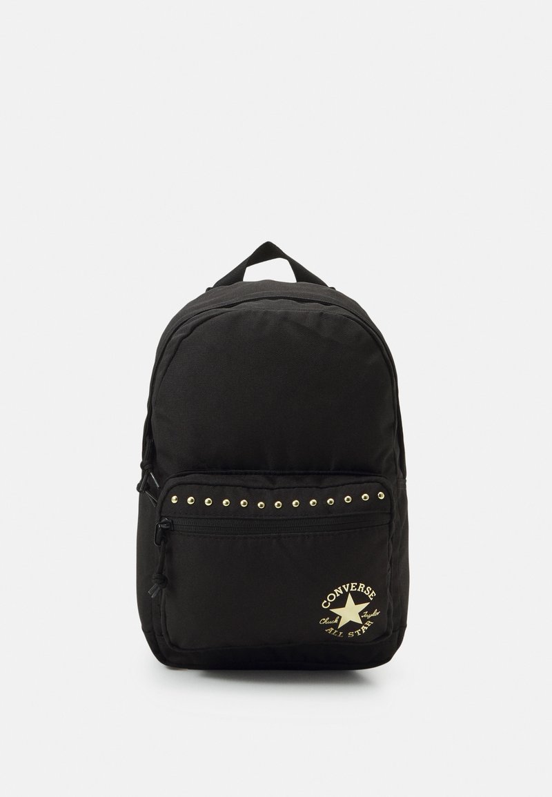 Sac à dos en tissu noir avec une poche frontale zippée ornée de clous dorés et d'un logo. Forme arrondie avec une poignée supérieure pour le transport.