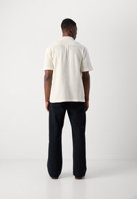 Maglietta a maniche corte color crema in maglia con una trama a rilievo, abbinata a pantaloni larghi blu navy scuri. Design minimalista, senza motivi visibili.