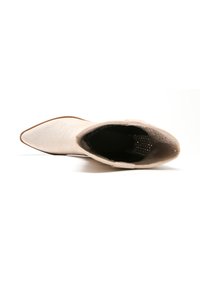 Botín beige hasta el tobillo con punta afilada, textura de ante suave y un sutil detalle de costura a lo largo de la parte superior, con un forro interior oscuro.