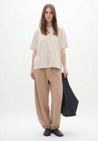 Beige oversized t-shirt, vida beige byxor, svart väska i handen och bruna skor. Mjukt tyg, avslappnad passform, minimal design.