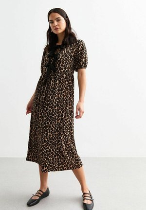 Robe midi imprimée léopard avec des manches courtes à volants, un détail à nouer noir au niveau du col et une coupe décontractée. Portée avec des chaussures plates noires.