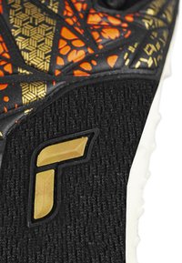 Svart sportskor med strukturerad ovandel, orange och guldigt geometriskt mönster, och guldig logotypdetalj. Gummisula med små knottrar för grepp.