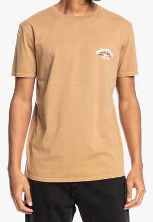 Camiseta de manga corta y cuello redondo en algodón de color marrón claro. Presenta un pequeño gráfico blanco en el pecho. Textura suave con un corte holgado.