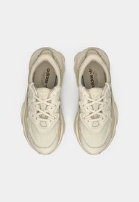 Ett par beige Adidas-sneakers med texturerad sömnad, tjocka sulor och korsade snören, vyda uppifrån på en vit bakgrund.