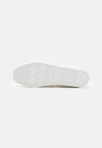 Witte sneakersole met getextureerde rubberen grip patronen en 'TOMS' branding. Heeft een glad oppervlak en een ronde neuzenontwerp.