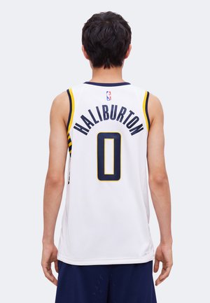 Persona de espaldas vistiendo una camiseta de baloncesto blanca con "Haliburton" y el número 0 en azul marino y ribete amarillo.