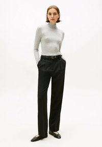 Grauer langärmeliger Rollkragenpullover kombiniert mit schwarzen maßgeschneiderten Hosen, die über einen Gürtel und Taschen verfügen. Glattes Material mit taillierter Passform.