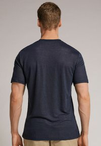 Námořnická modrá tričko s krátkým rukávem vyrobené z měkké tkaniny; obsahuje klasický kulatý výstřih a jemnou melírovanou strukturu na zádech.