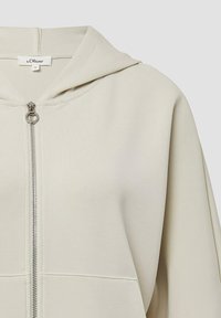 Helle beigefarbene Kapuzensweatjacke mit einem Frontreißverschluss, aus weichem Stoff, mit lockerer Passform und ohne sichtbare Muster oder Verzierungen.