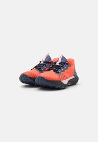 Zapatillas de trail running con un upper vibrante en naranja, acentos en negro y marino, malla transpirable, suela gruesa negra y detalles reflectantes.