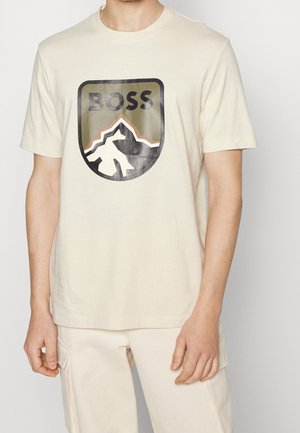T-shirt en coton couleur crème avec un grand logo graphique noir, vert et blanc représentant une montagne, accompagné du texte "BOSS". Encolure arrondie.