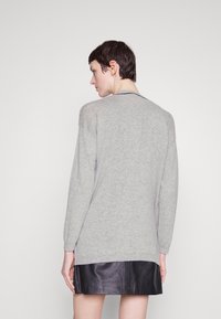 Pull gris avec une coupe décontractée, des manches longues et un col rond, associé à une jupe en cuir noir. Texture douce et design minimaliste.