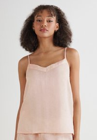 Top sin mangas de color rosa claro con escote en V y tirantes finos. Hecho de una tela suave y texturizada, con un ajuste holgado y un diseño minimalista.
