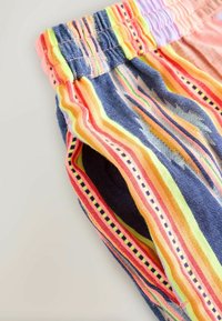 Bukser med elastik i taljen og flerfarvede lodrette striber i blå, orange, gul, rød og lilla stof.