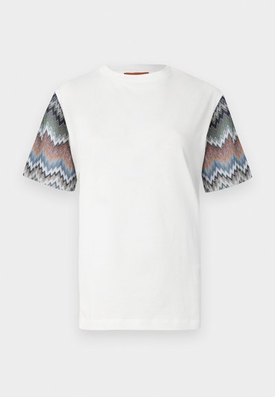Bela majica s kratkimi rokavi s vzorcem večbarvnih cikcak črt. Mehka tekstura, okrogel izrez in ohlapna prileganje.