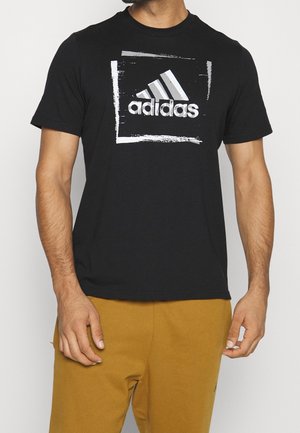Černé bavlněné tričko s bílým logem Adidas v obdélníkovém designu štětcem na přední straně. Krátké rukávy, kulatý výstřih.