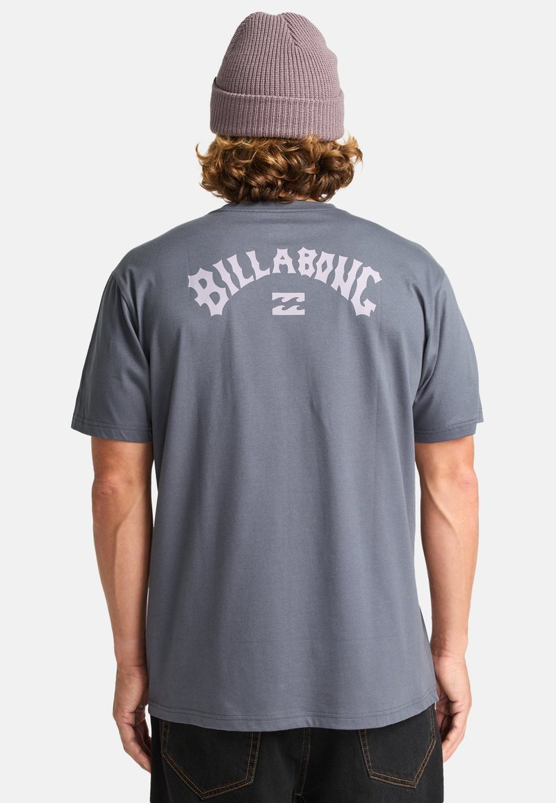 Sivý bavlnený tričko s logom "BILLABONG" v svetloružovej farbe na chrbte, krátke rukávy a voľný strih. Nosí sa s rebrovanou čiapkou.