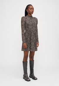 Robe à imprimé léopard avec des manches longues et un col montant, en tissu doux, associée à des bottes grises hauteur genou avec des accents de boucle.