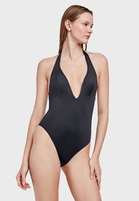 Bañador negro de una pieza con escote en V profundo, tirantes halter y piernas altas; hecho de un material suave y elástico.