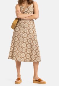 Ruskea kuvioitu mekko, jossa on valkoisia kukkakuvioita, ohuet olkaimet ja levenevä hame. Yhdistetty vaaleanruskeisiin korkokenkiin ja olkalaukkuun.