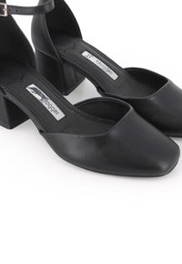 Zapatos de cuero negro con tacones cuadrados y correas en el tobillo, con etiqueta "blogger" en el interior.