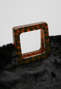 Sköldpaddsmönstrad fyrkantig handtag fäst vid en kropp av svart konstläder, med en slät yta och blank finish.