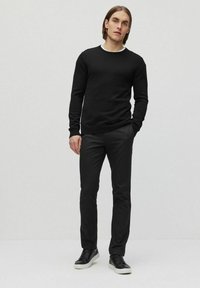 Zwarte gebreide trui met een ronde hals, gecombineerd met slim-fit zwarte broek en zwarte sneakers met witte zolen. Eenvoudig en monochroom ontwerp.