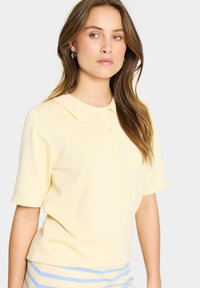 Polo en tissu jaune doux, avec un col classique et des manches courtes roulées, doté de détails de patte de boutonnage à l'avant.