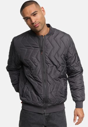 Veste bomber matelassée en gris foncé, avec fermeture éclair à l'avant, poignets et ourlet côtelés, et motif en chevrons pour une texture supplémentaire.