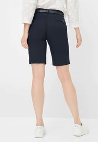 Marineblauwe shorts van soepel stof, met een tailored fit, twee achterzakken en een opgerolde zoom, gecombineerd met witte sneakers.
