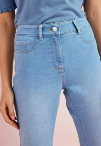 Jeans taille haute de couleur bleu clair en denim. Les caractéristiques incluent des poches avant, un bouton en argent et des détails de couture subtils.