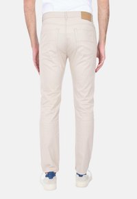 Pantaloni beige slim-fit realizzati in cotone, con tasche posteriori e un'etichetta in pelle marrone sulla vita. Texture liscia con dettagli minimi.