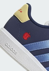 Marinblå sneaker med en texturerad vit sula, med ljusblå ränder och en röd broderad äpplelogotyp på sidan, gul hälackent.