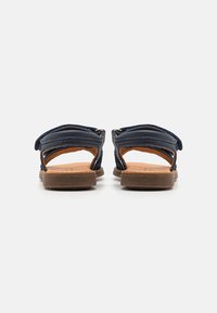 Mørkeblå sandaler med justerbare stropper, åpen bakdesign, flat brun såle og teksturerte stoffpaneler.