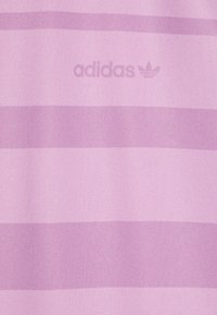 Gaiši purpura audums ar tumšāk purpura horizontālām svītrām. Uz tā ir Adidas logo smalkā drukā. Strukturēta virsma.
