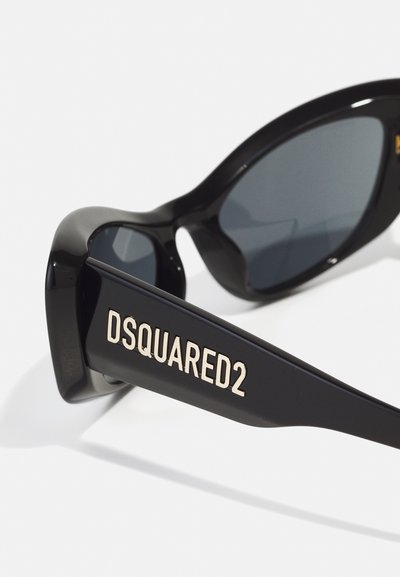Black sunglasses with a bold, chunky frame, dark lenses, and a matte finish. DSQUARED2 in gold lettering on the side arm.