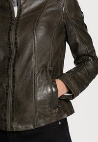 Brązowa skórzana kurtka o gładkiej, błyszczącej fakturze, z zamek z przodu, kieszeniami bocznymi i subtelnymi detalami szycia.